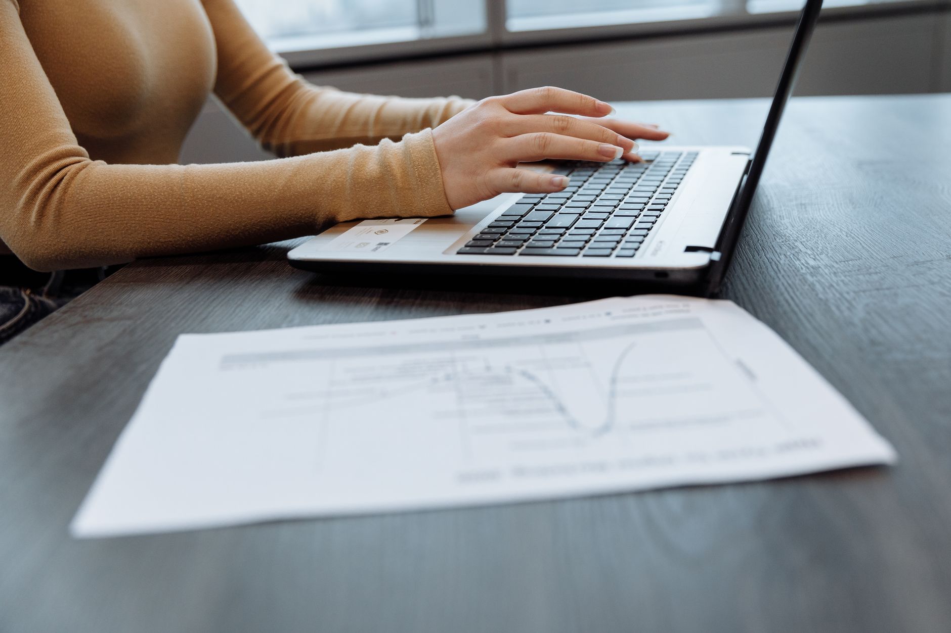 Mains posées sur le clavier d’un ordinateur portable, documents de travail à côté.